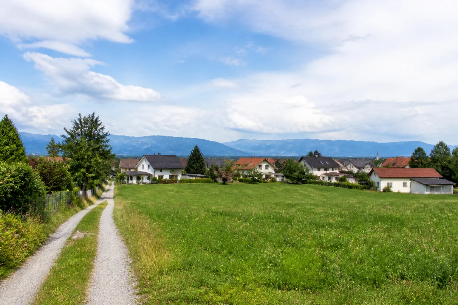 Offene österreichische Grundstücksparzelle mit Weg und Siedlung im Hintergrund